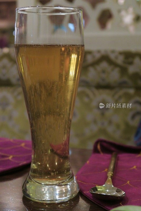 在餐厅的桌子上拍摄的大杯啤酒的照片，上面有餐垫、餐具/模糊的背景